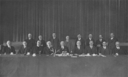 Aan de bestuurstafel op de Algemeene Vergadering van 5 Januari 1934.
Van l. naar r., zittend: de heren ten Seldam, Dr. Kruisinga, Prof. Dr. Gerlach Roven, insp. Bolkestein, Dr. van den Ent, Dr. Ras, Lieve, Prof. Dr. van Dam, insp. Dr. Elzinga. Staand: de heren insp. van Andel, insp. Dr. van Swaay, Dr. Sparnaay, Dr. Zijderveld, Dr. de Liefde, W. Kramer, Prof. Dr. de Vooys, Dr. Schepman.